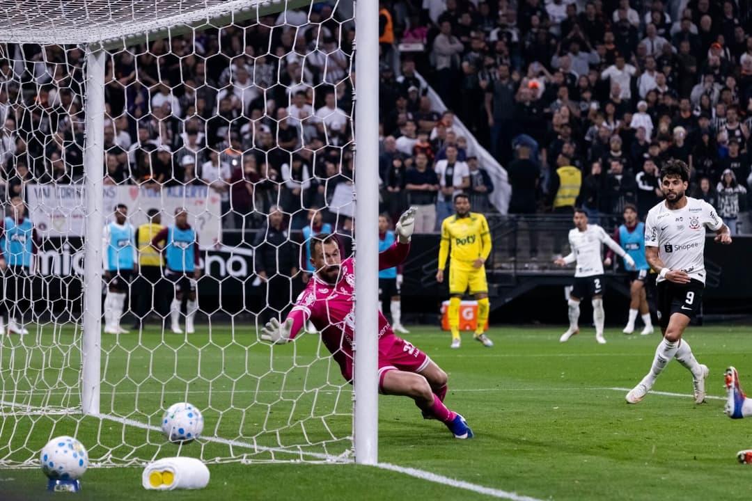 Corinthians em campo: goleiro de uniforme rosa faz defesa junto à trave enquanto atacante branco avança com a bola.