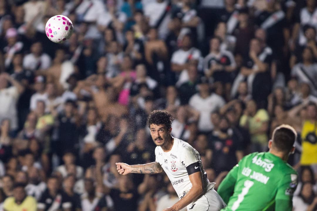 Jogador do Corinthians em ação durante partida, com bola no ar e goleiro adversário ao fundo.