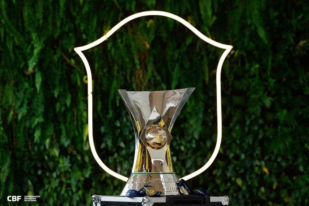 Taça Brasileirão em pedestal prateado, com moldura neon ao fundo e logotipo da CBF.
