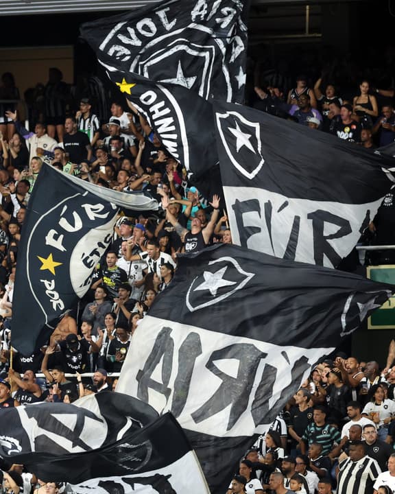 Torcida do Botafogo agita bandeiras pretas e brancas com o escudo estrelado no estádio.