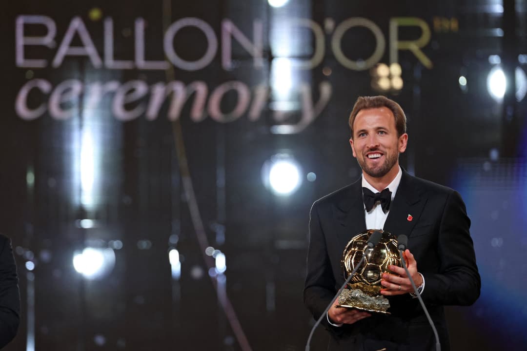 Homem de terno preto no palco segurando o troféu Ballon d'Or na cerimônia.