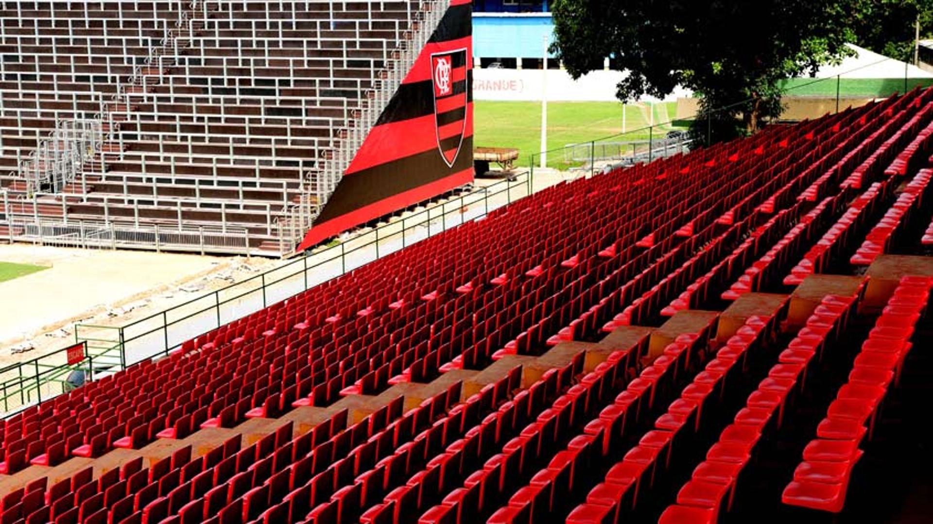 Cadeiras em vermelho na tribuna e setor Sul (espaço dos visitantes), ao fundo, com símbolo do Flamengo