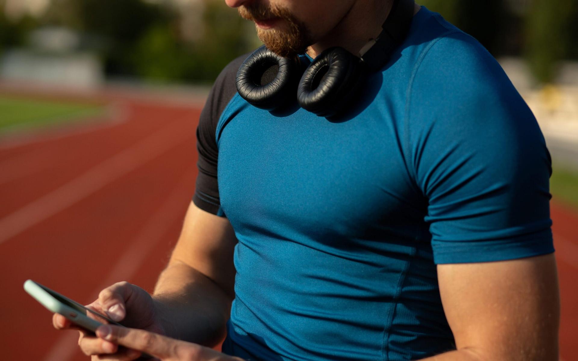 closeup-tiro-de-um-jovem-atleta-com-fones-de-ouvido-no-pescoco-digitando-mensagem-de-texto-em-seu-telefone-celular-scaled-aspect-ratio-512-320