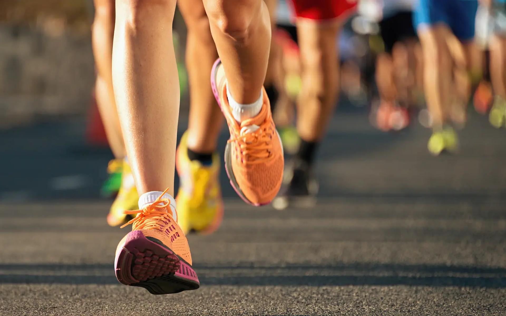 zoom nos pés de corredores em uma prova de rua, com foco em um par de tênis laranja