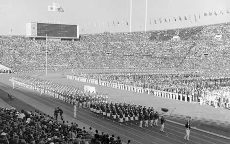 Diante das arquibancadas lotadas do Estádio Nacional de Tóquio, a delegação do Japão desfila na cerimônia de abertura dos Jogos de Tóquio-1964 (Crédito: COI)
