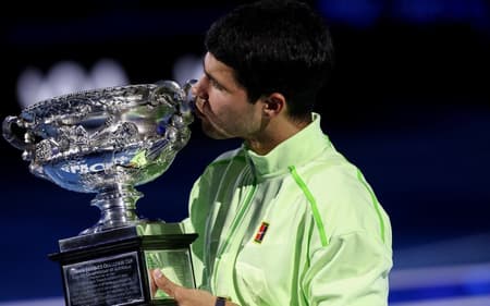 O espanhol Carlos Alcaraz beija seu sétimo Grand Slam, o primeiro no Australian Open (Foto: IZHAR KHAN / AFP)