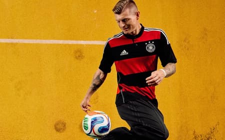 Toni Kroos utilizando a camisa rubro-negra da Aleamanha, em listras horizontais, e erguendo uma bola com o calcanhar do pé