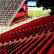 Cadeiras em vermelho na tribuna e setor Sul (espaço dos visitantes), ao fundo, com símbolo do Flamengo