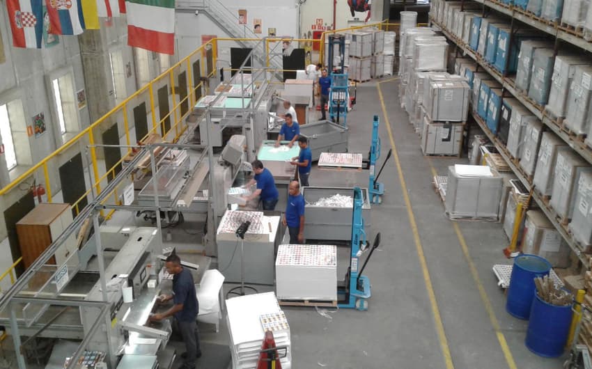 GALERIA: A fábrica da Panini em imagens. Na foto, homens trabalham nas guilhotinas que cortam as figurinhas em blocos
