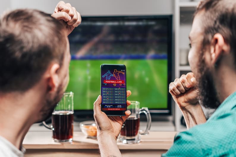 Two male friends watching live football game broadcast on tv