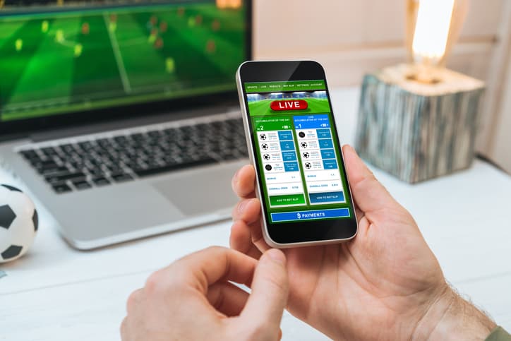 Man watching soccer play online broadcast on his laptop, cheering for favourite team, making bets using mobile application