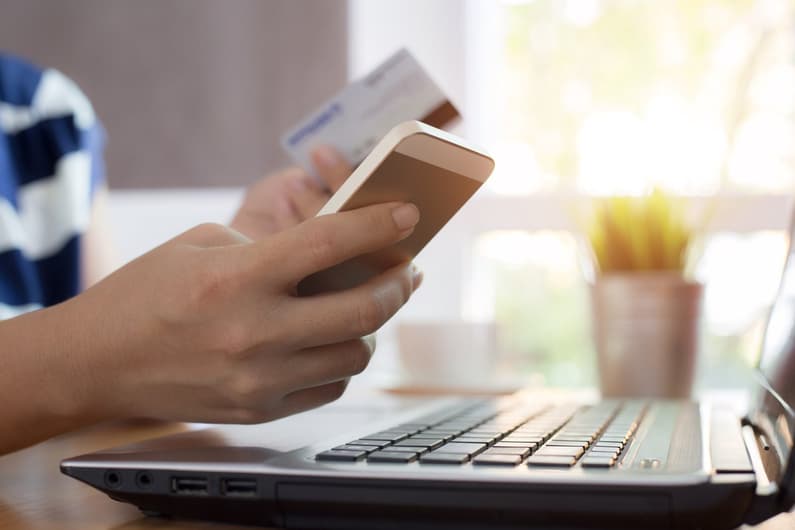 Woman hands holding credit card and using smart phone with laptop computer Online shopping concept