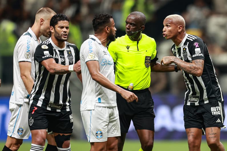 Deyverson jogador do Atletico-MG disputa lance com Reinaldo jogador do Gremio e o Arbitro Luiz Flavio de Oliveira durante partida no estadio Arena MRV pelo campeonato Brasileiro A 2024. Foto: Gilson Lobo/AGIF