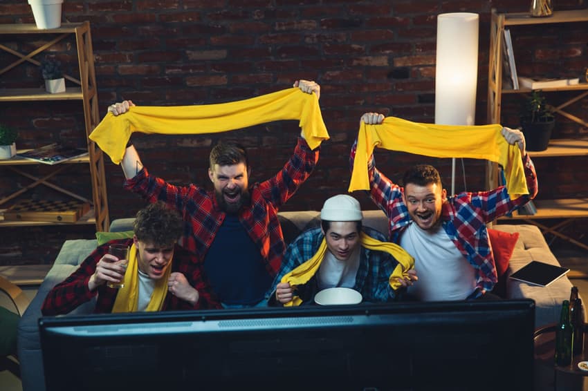 Group of friends watching TV, sport match together. Emotional fans cheering for favourite team, watching on exciting game. Concept of friendship, leisure activity, emotions