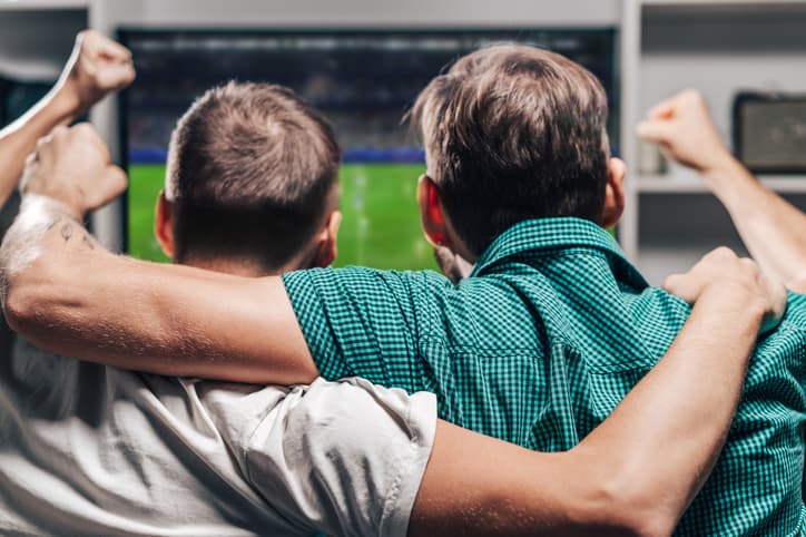 Two male friends watching live football game broadcast on tv