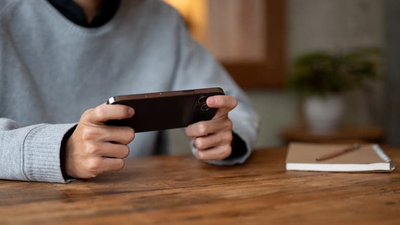 A man playing a mobile game or watching a video on his smartphone while relaxing in a coffee shop.