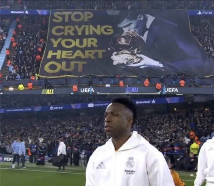 Vini Jr perfilado para a partida enquanto torcida do City ergue faixa provocativa (Foto: Reprodução/X)