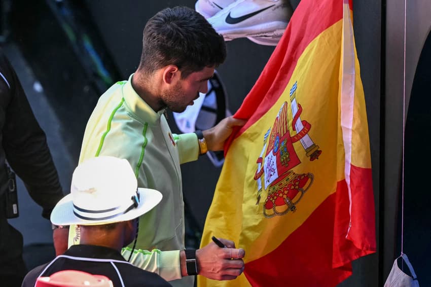 Carlos Alcaraz, da Espanha, autografa bandeira espanhola após vencer o francês Corentin Moutet no Aberto da Austrália, em Melbourne, em 23 de janeiro de 2026 (Foto: William West/AFP)