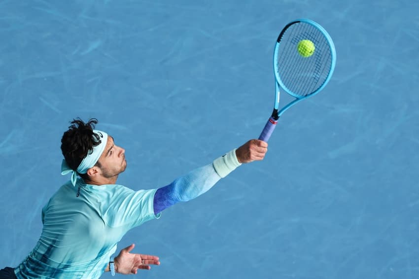 O italiano Lorenzo Musetti saca na partida contra Novak Djokovic no Australian Open (Foto: Martin KEEP / AFP)