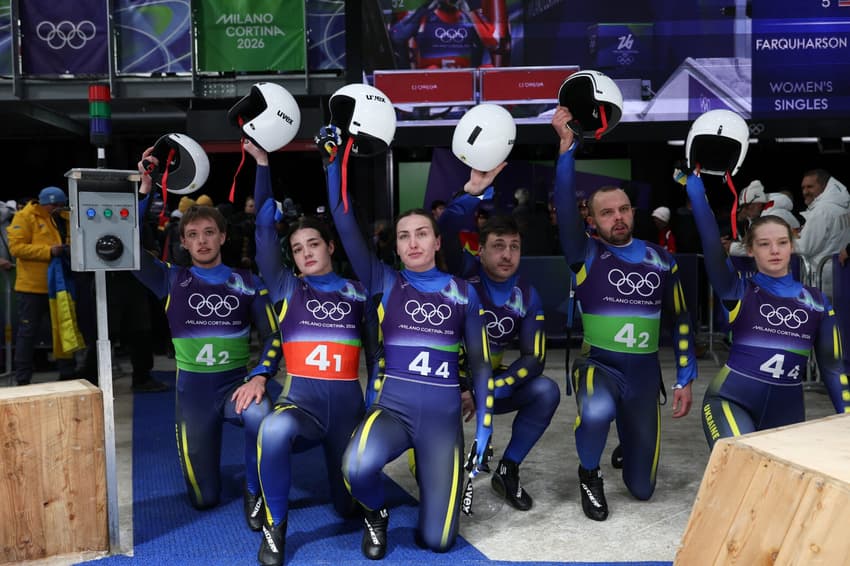 Ihor Hoi, Yulianna Tunytska, Oleksandra Mokh, Andriy Mandziy, Nazarii Kachmar e Olena Stetskiv, da Ucrânia, ajoelham-se após o revezamento misto por equipes do luge no Cortina Sliding Centre, nos Jogos Olímpicos de Inverno Milano Cortina 2026, em 12 de fevereiro de 2026. (Foto: Franck Fife/AFP)