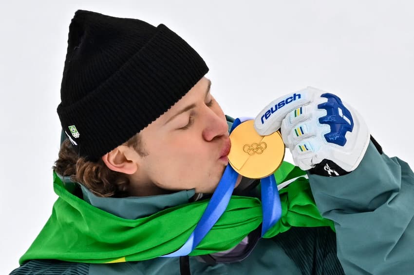 Lucas Pinheiro Braathen beija a medalha de ouro no pódio do slalom gigante masculino em 2026. (Foto: Fabrice Coffrini/AFP)