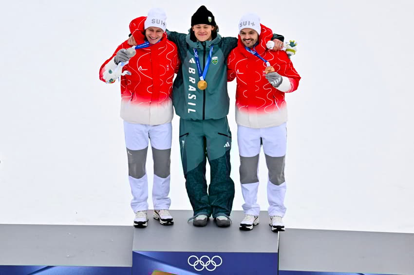 Da esquerda para a direita, Marco Odermatt (prata), Lucas Pinheiro Braathen (ouro) e Loic Meillard (bronze) celebram no pódio do slalom gigante masculino em 2026. (Foto: Fabrice Coffrini/AFP)
