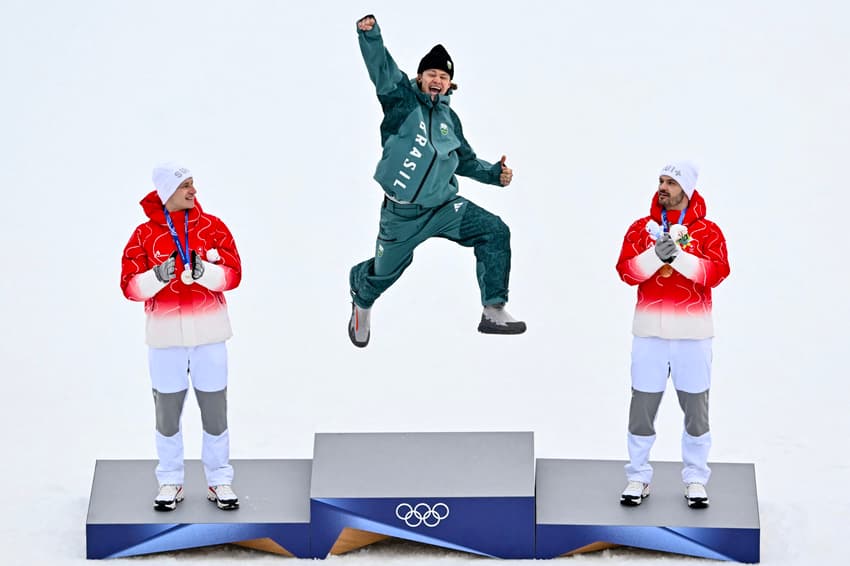 Da esquerda para a direita, Marco Odermatt (prata), Lucas Pinheiro Braathen (ouro) e Loic Meillard (bronze) celebram no pódio do slalom gigante masculino em 2026. (Foto: Fabrice Coffrini/AFP)