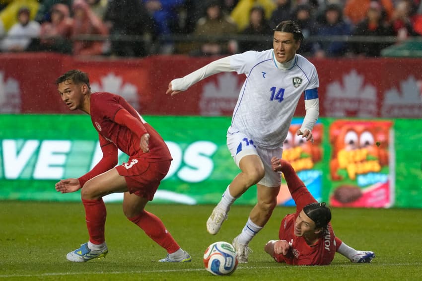 O atacante Shomurodov disputa a bola com dois defensores do Canadá; veterano é o segundo jogador mais valioso do time (Foto Jeff Vinnick / AFP)