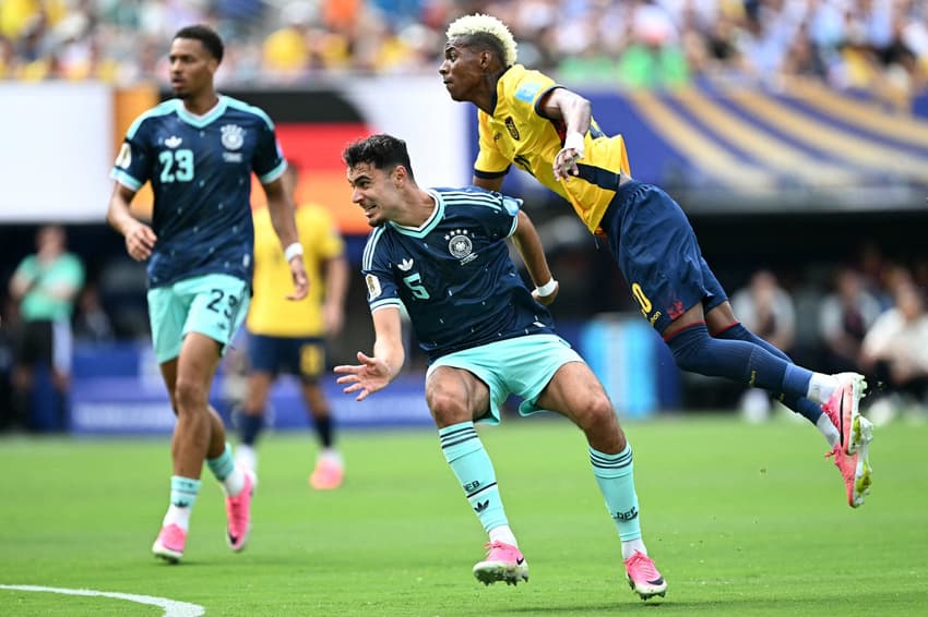 Pressionado pela marcação de Pavlovic, trajando o novo uniforme azul da Alemanha, Angulo finaliza para abrir o placar para o Equador na Copa do Mundo