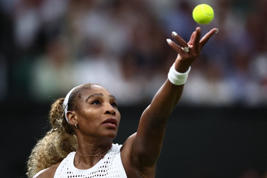 De faixa branca na cabeça e top branco, Serena Williams lança a bola com a mão esquerda para sacar em partida de Wimbledon