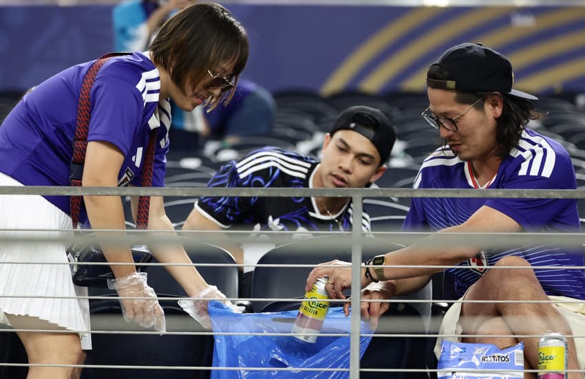 De camisas azuis, torcedores do Japão seguram um saco de lixo azul e recolhem resíduos na arquibancada após o jogo contra a Suécia pela Copa do Mundo