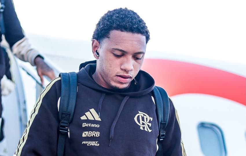 Daniel Sales descendo do avião com fone no ouvido e moletom marrom