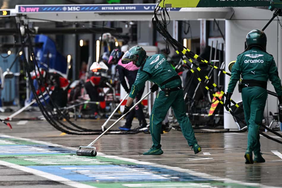 Mecânicos da Aston Martin passam o rodo tentando secar a entrada dos boxes (foto: Andrej ISAKOVIC / POOL / AFP)