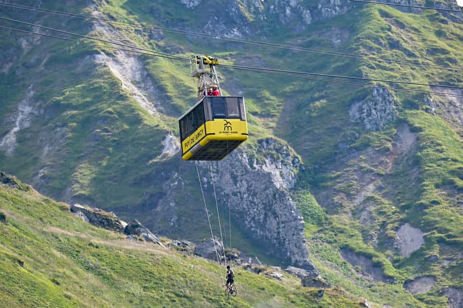 Um ciclista se pendura em uma gôndola na área de chegada no topo do Mont-Dore Puy de Sancy durante a 10ª etapa da Tour de France 2025 (foto: Loic VENANCE / AFP)