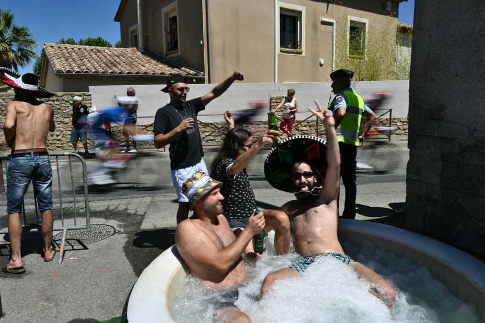Os ciclistas passam a fundo enquanto espectadores se refrescam em uma piscina inflável (foto: Marco BERTORELLO / AFP)