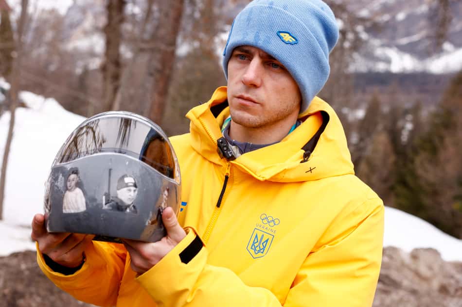 O ucraniano Vladyslav Heraskevych segura o capacete com imagens de vítimas da guerra com a Rússia, em Cortina d'Ampezzo, em 12 de fevereiro de 2026. Ele foi desclassificado dos Jogos por descumprir as diretrizes de expressão do COI. (Foto: Odd Andersen/AFP)