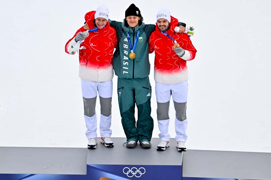 Da esquerda para a direita, Marco Odermatt (prata), Lucas Pinheiro Braathen (ouro) e Loic Meillard (bronze) celebram no pódio do slalom gigante masculino em 2026. (Foto: Fabrice Coffrini/AFP)