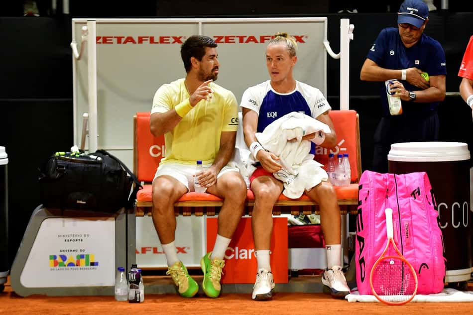Sentados em um banco, Rafael Matos e Orlando Luz conversam durante pausa em jogo do Rio Open