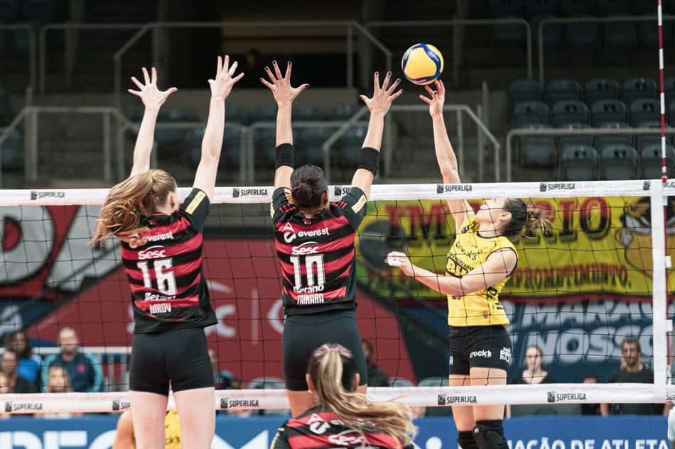 Michelle Pavão, do Praia Clube, ataca contra o bloqueio duplo do Sesc RJ Flamengo, formado por Masa Kirov e Simone Lee, em jogo válido pela Superliga Feminina 2025/26