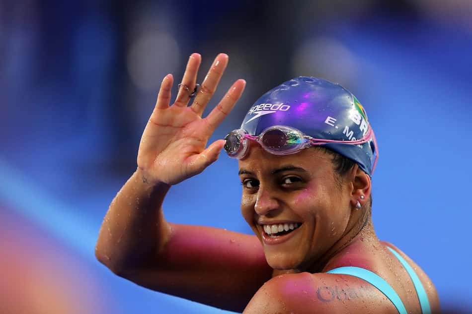 De touca e óculos, Etiene Medeiros acena para trás e sorri