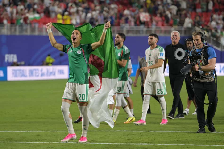 O atacante Adil Boulbina comemora com a bandeira da Argélia a classificação do país junto com companheiros após o empate com a Áustria na Copa do Mundo