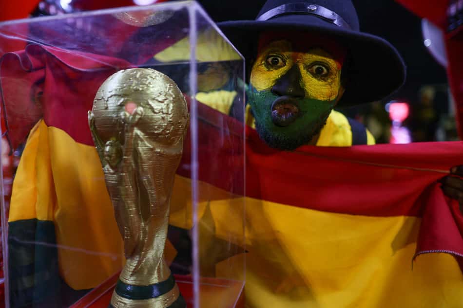 Torcedor de Gana com o rosto pintado e segurando a bandeira comemora a classificação do país em frente a uma réplica da taça da Copa do Mundo