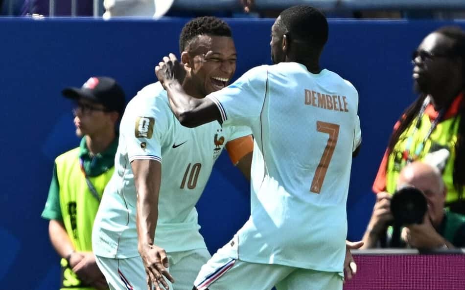 Dembélé e Mbappé, de camisas brancas, se abraçam e comemoram o terceiro gol da França contra a Noruega
