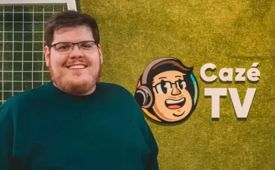 Casimiro Miguel sorri em frente ao logotipo do seu canal CazéTV