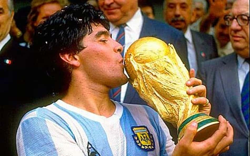 Maradona, com a camisa azul e branca da Argentina, beija a taça da Copa do Mundo de 1986