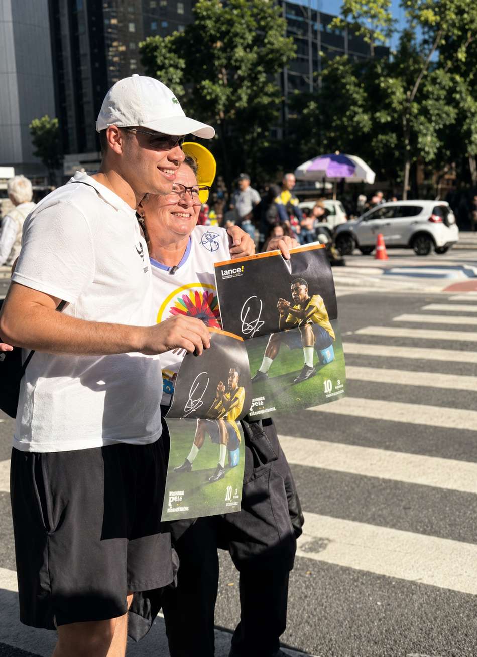 Casal de boné mostrando a parte autografada de Pelé do Manual do Torcedor do Lance!