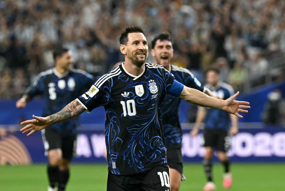 De camisa preta com detalhes em azul, Messi comemora, de abraços abertos, o gol marcado contra a Jordânia na Copa do Mundo