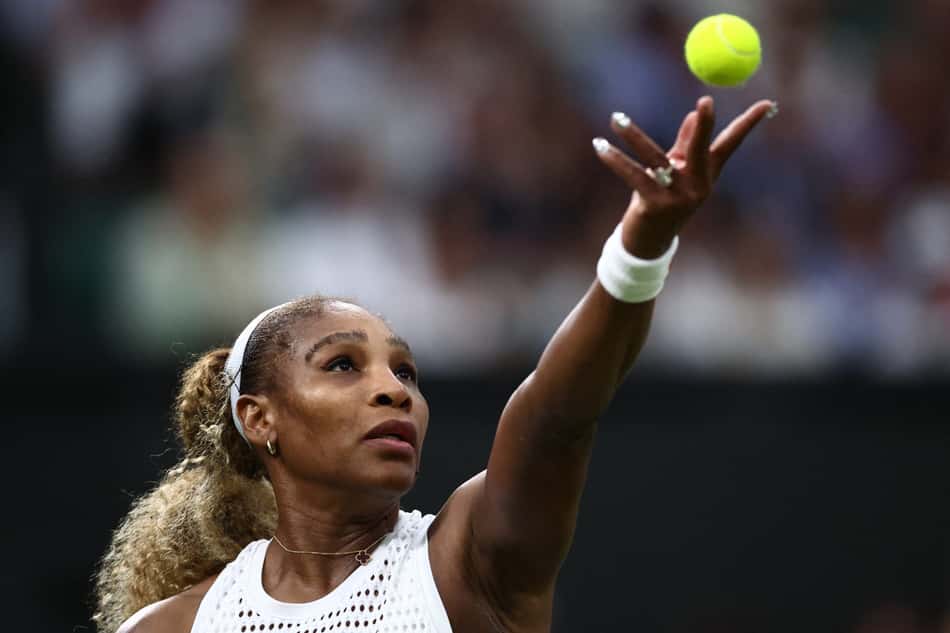 De faixa branca na cabeça e top branco, Serena Williams lança a bola com a mão esquerda para sacar em partida de Wimbledon