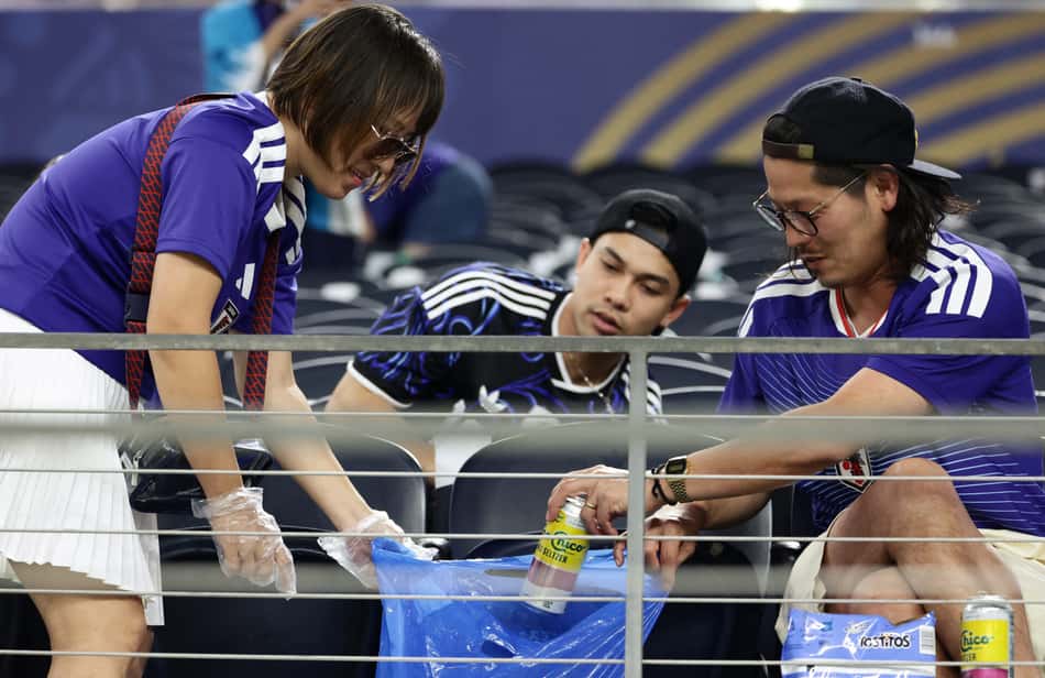 De camisas azuis, torcedores do Japão seguram um saco de lixo azul e recolhem resíduos na arquibancada após o jogo contra a Suécia pela Copa do Mundo