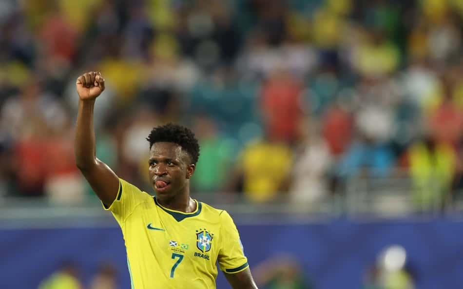Vinicius Junior, de amarelo, levanta a mão direita em direção ao céu